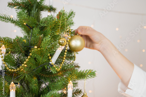 Close up of woman decorating christmas tree with goldenChristmas baubles. Copy space over white wall with lights photo