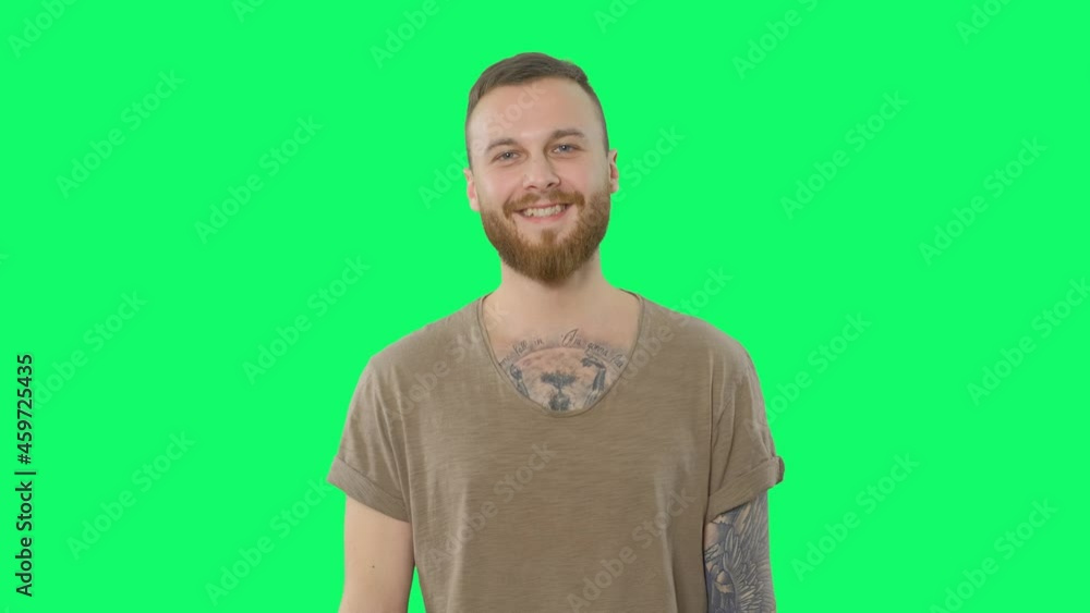 Happy handsome man on chroma key. Positive bearded tattooed hipster is looking to the camera and smiling on green screen background. Isolated portrait for keying Happy handsome man on chroma key. Positive bearded tattooed hipster is looking to the camera and smiling on green screen background. Isolated portrait for keying