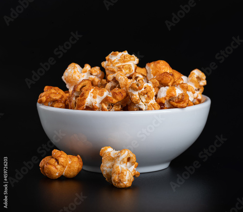 Sweet popcorn with caramel syrup in a white ceramic bowl on a glossy black background with reflection