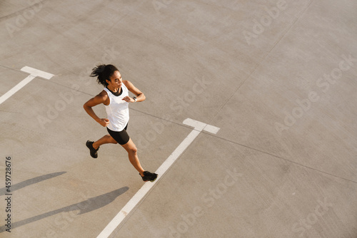 Black sportswoman running while working out on parking