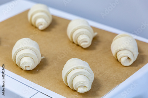 Croissants formed from raw dough lie on baking paper before being sent to the oven. Handmade pastry baking process