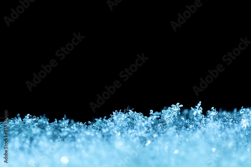 Natural snow texture with snowflakes close-up in soft blue tones on the window, isolated on black background with space for text. Blank for holiday gift cards. Macro texture of snow.