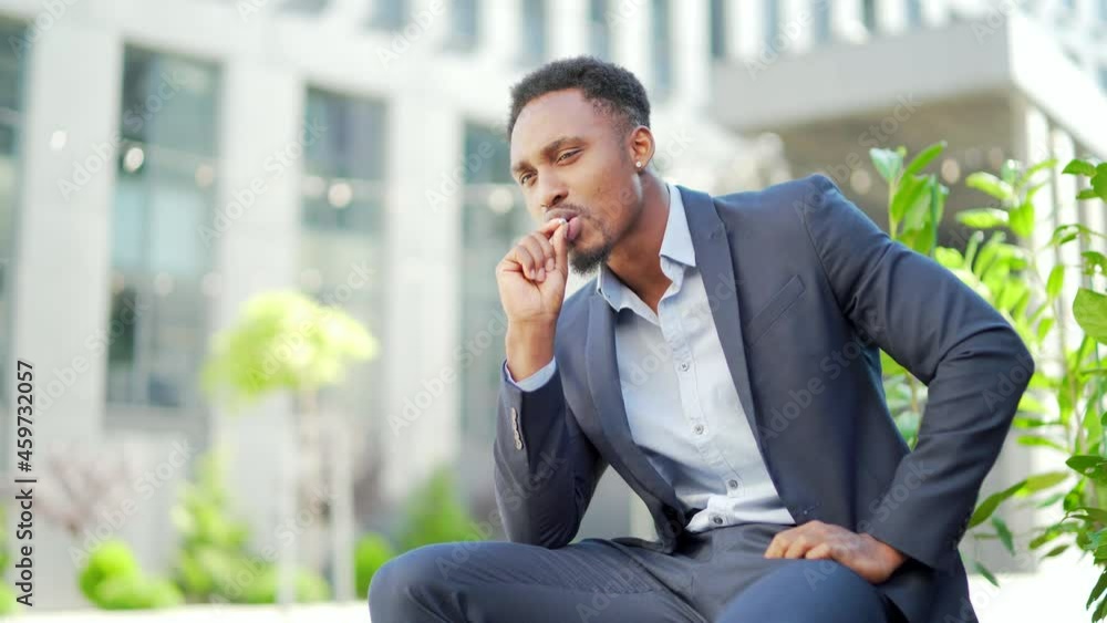 african american business man smoking cannabis outdoors sitting on city park bench on urban street background. Male employee Businessman. Office worker in suit Relieves stress a marijuana outside african american business man smoking cannabis outdoors sitting on city park bench on urban street background. Male employee Businessman. Office worker in suit Relieves stress a marijuana outside