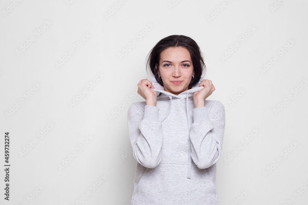 Young woman brunette in a light grey sweater with hood, looking at camera isolated on white background. Space copy. Young woman brunette in a light grey sweater with hood, looking at camera isolated on white background. Space copy.
