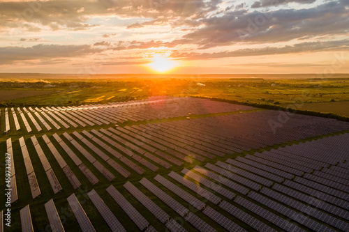 Aerial view of large sustainable electrical power plant with many rows of solar panels for producing clean ecological electric energy at sunset. Renewable electricity with zero emission concept.