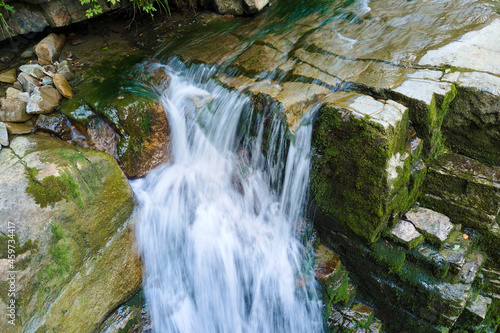 Fototapeta Naklejka Na Ścianę i Meble -  Waterfall on mountain river with white foamy water falling down from rocky formation in summer forest.