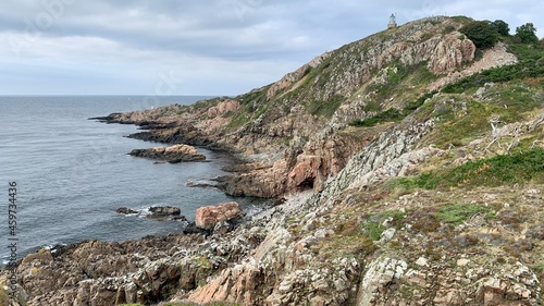 Felsige Küstenlandschaft in Südschweden mit rotem Gestein, Leuchtturm, Segelbooten, Häuschen und Bäumen