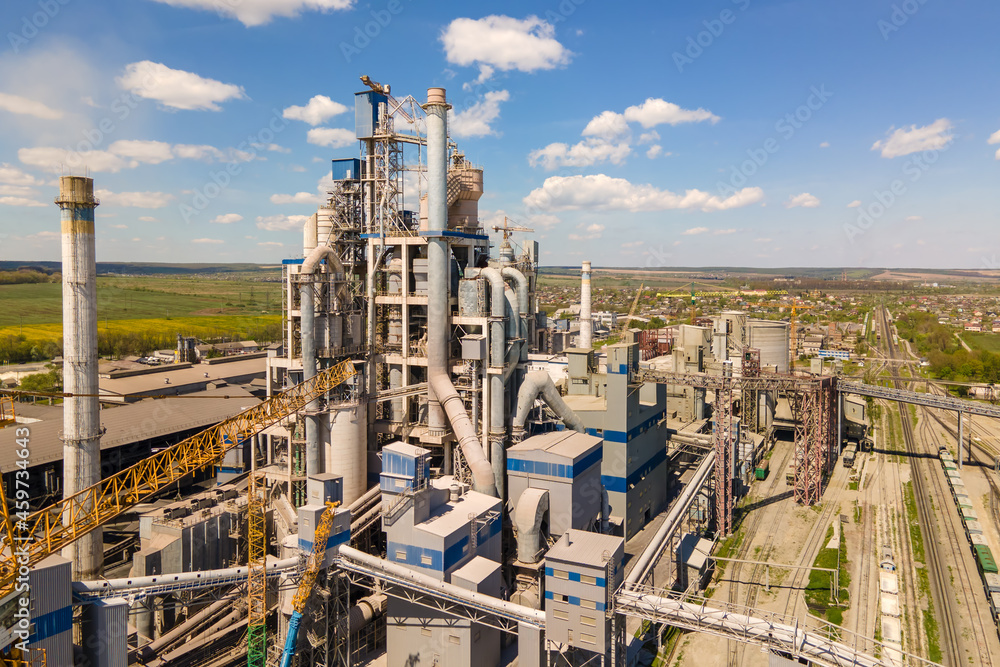 Fototapeta premium Aerial view of cement plant with high concrete factory structure and tower crane at industrial production area. Manufacture and global industry concept.