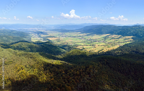 Aerial view of mountain hills covered with dense green lush woods on bright summer day.