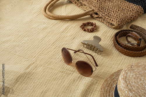 Aesthetic bohemian fashion women's accessories on muslin cloth background. Summer holidays, vacation, travel concept. Straw hat, bag, sunglasses, leather belt, barrette