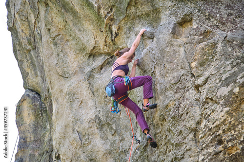 Determined girl climber clambering up steep wall of rocky mountain. Sportswoman overcoming difficult route. Engaging in extreme sports and rock climbing hobby concept.