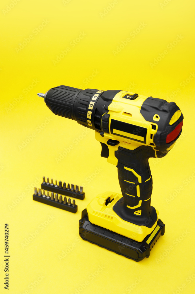 Fototapeta premium The yellow-black screwdriver on a yellow background, a set of bits.