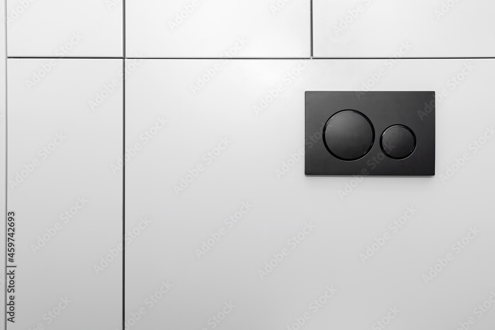 Black matt toilet flush with two round buttons placed in the wall of a restroom lined with a wooden panel. Black matt toilet flush with two round buttons placed in the wall of a restroom lined with a wooden panel.