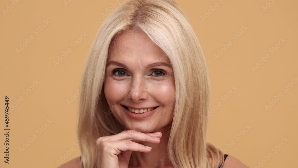 A close-up view of the smiling mature beautiful woman looking at the camera in the beige studio A close-up view of the smiling mature beautiful woman looking at the camera in the beige studio