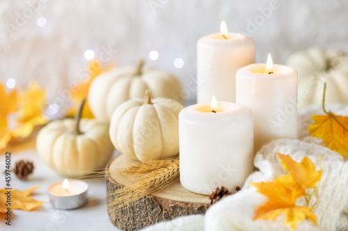 Hello Autumn or Happy Thanksgiving concept. White burning candles with white pumpkins at the background  knitted plaid and autumnal leaves. Shallow depth of field
