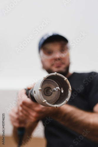 Construction worker electrician or plumber wearing a protective mask with a hammer drill and drill bit bit on concrete - bottom view focus on the drill
