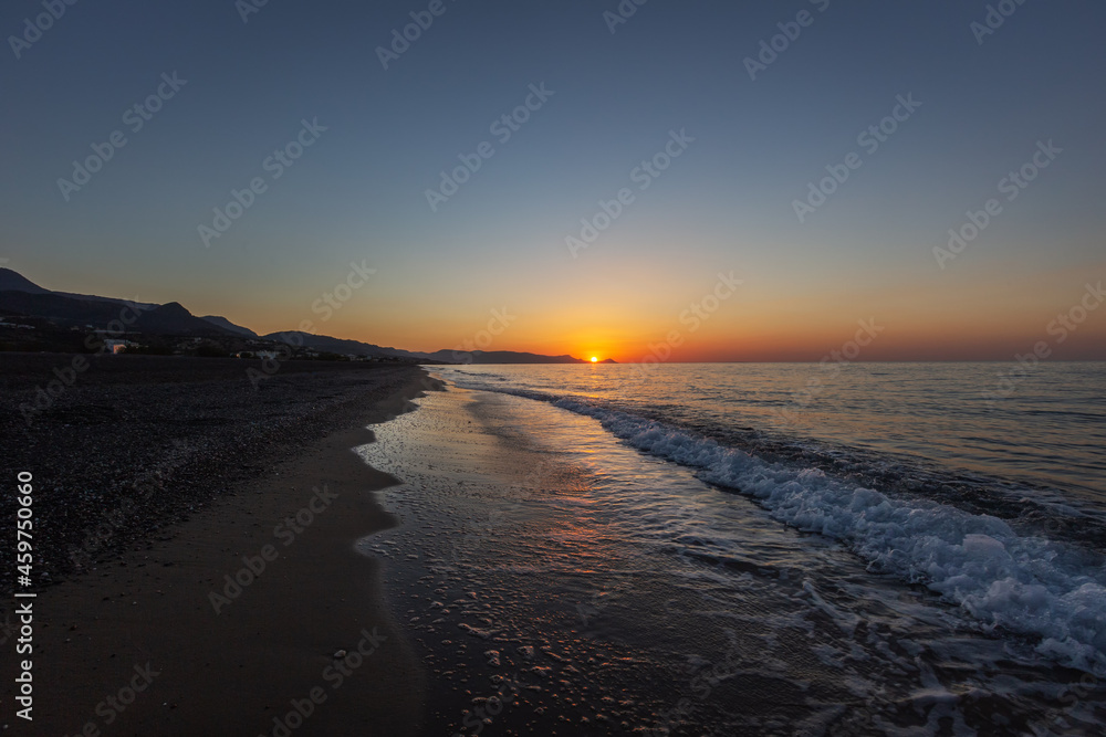 Fototapeta premium Sandy beach at sunrise with beautiful sea waves in the background of mountain and beautiful colorful sky with sun