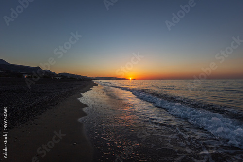 Sandy beach at sunrise with beautiful sea waves in the background of mountain and beautiful colorful sky with sun