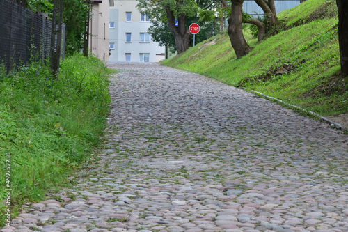 A road paved with stones uphill among grasses and trees. Summer. Day.