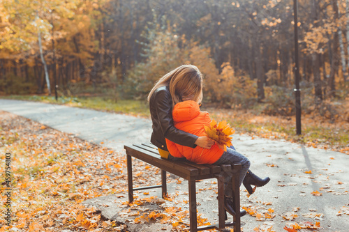 Single parent mother and child boy in the autumn in park sit on bench. Fall season and family concept.