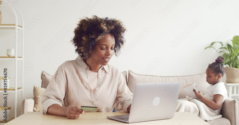 Young african woman paying online with credit card and laptop, buying toys for her daughter on ecommerce website Young african woman paying online with credit card and laptop, buying toys for her daughter on ecommerce website