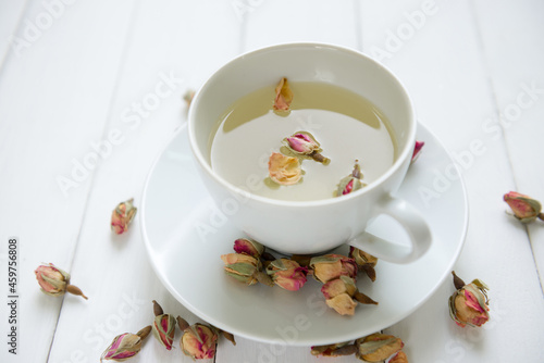 Aromatic and soothing hot rose tea served in a cup. Dried rose buds scattered around cup of herbal tea.