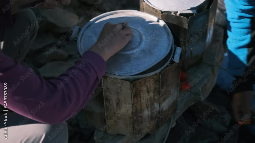 The girl covers a large saucepan with boiled porridge with a lid while cooking in the mountains. Cooking lunch during the hike. The cook prepares lunch at the camp for a group of tourists. The girl covers a large saucepan with boiled porridge with a lid while cooking in the mountains. Cooking lunch during the hike. The cook prepares lunch at the camp for a group of tourists.