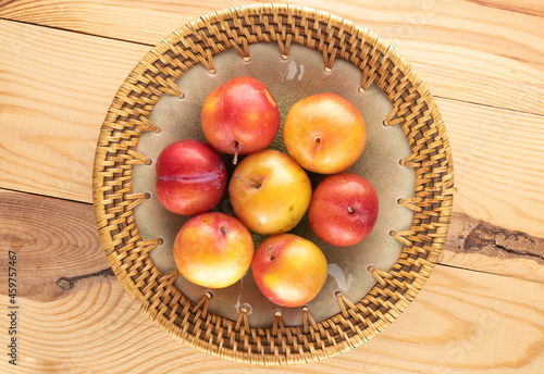 Several juicy sweet yellow-red plums on a ceramic dish on a wooden table, close-up, top view.