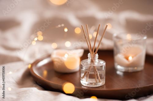 Home perfume in glass bottle with wood sticks, scented burn candles  tray in bedroom close up. Aromatherapy cozy atmosphere lifestyle. Winter warm xmas season.