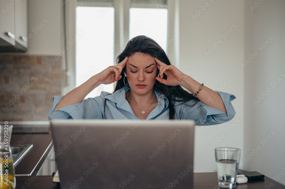 Tired businesswoman having a headache while in her home office working on a laptop Tired businesswoman having a headache while in her home office working on a laptop