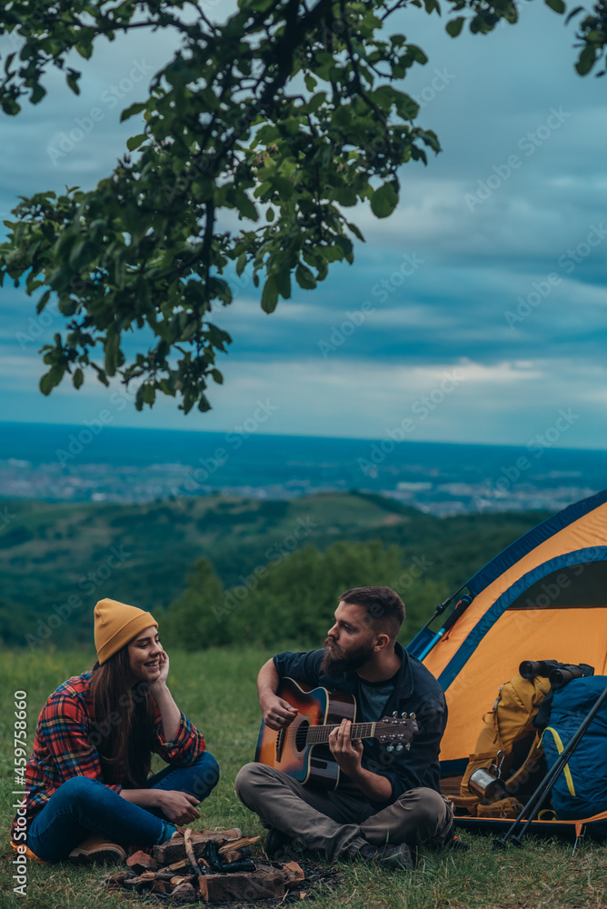 Couple of campers sitting by the camp tent and playing guitar Couple of campers sitting by the camp tent and playing guitar