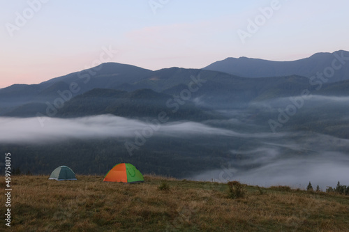 Picturesque view of mountain landscape with fog and camping tents in early morning