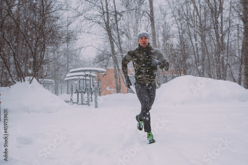 Training outside in winter in a snowfall. a man runs during a snowstorm. There is a winter park against the background, it is snowing, there are bare trees