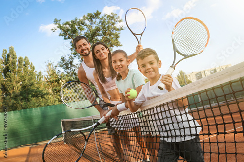 Happy family with tennis rackets on court outdoors © New Africa