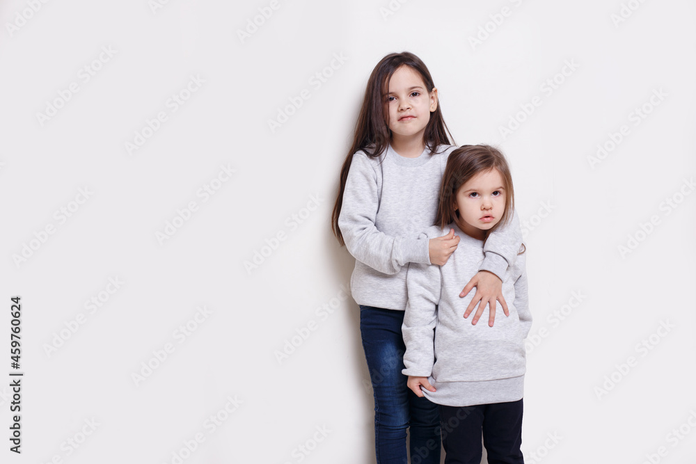 Two adorabile littel girl in sweater and jeans, posing together on white background, smiling and looking at camera. Two adorabile littel girl in sweater and jeans, posing together on white background, smiling and looking at camera.