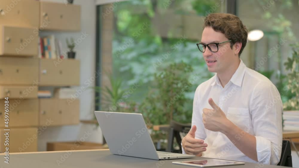Young Man Talking on Video Call on Laptop in Modern Office