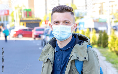 Portrait of a young man in a protective mask on his face against the background of the city. Quarantine.
