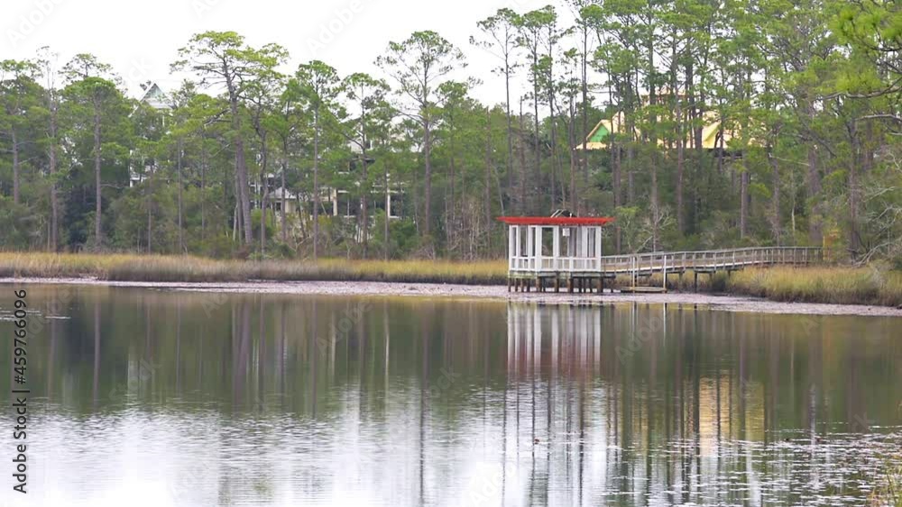 Landscape nature view on Western lake park by Gulf of Mexico in Seaside, Florida on cloudy weather with wooden boardwalk and houses reflection in winter Landscape nature view on Western lake park by Gulf of Mexico in Seaside, Florida on cloudy weather with wooden boardwalk and houses reflection in winter