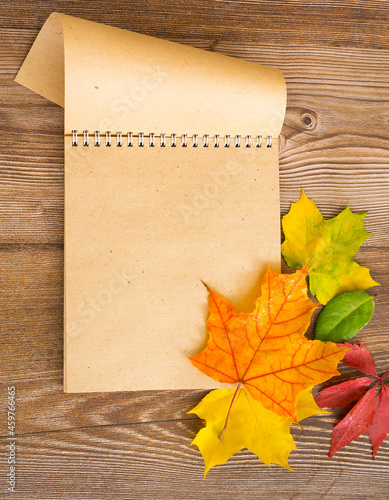 Opened notebook on a wooden background. Colored autumn leaves lie nearby
