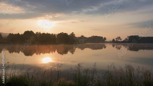 Beautiful sunrise at lake surrounded by forest. Morning fog floating over water surface. Birds singing in the background. Krasnobród, Roztocze, Poland.