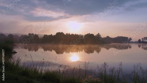 Beautiful sunrise at lake surrounded by forest. Morning fog floating over water surface. Birds singing in the background. Krasnobród, Roztocze, Poland.