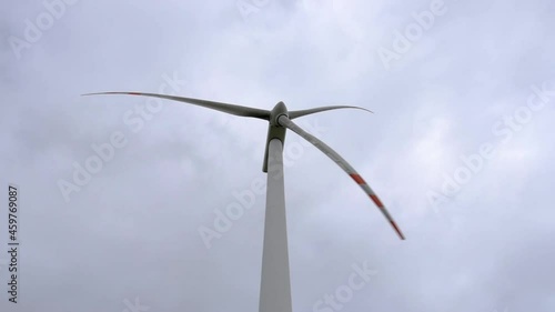 The windmill producing electricity in combination with the infrastructure for electricity transmission. Cloudy sky in the background.