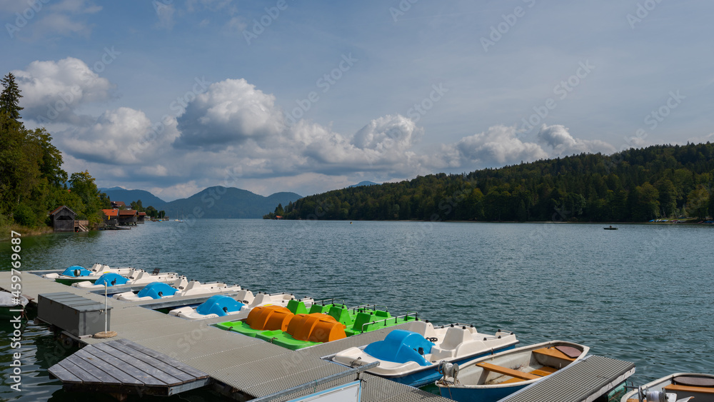 Rental pedal boats on pier at mountain lake Walchensee in Bavaria, Germany on sunny day with boat house