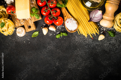 Italian food background on black. Raw Pasta, fresh tomatoes, olive oil, spices and basil. Top view with copy space.