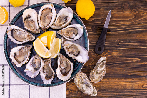 fresh oysters with lemon wedges on a blue platter with an oyster knife on a wooden background, with copy meta.