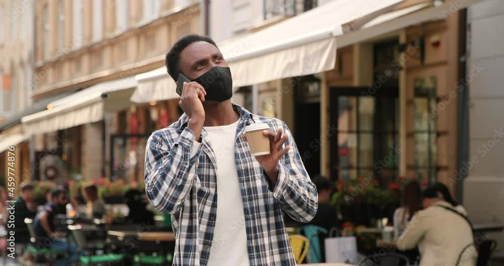 Multiracial man in medical mask standing on street and chatting on mobile phone. Male in respiratory protection is holding coffee and chatting. Pandemic concept Multiracial man in medical mask standing on street and chatting on mobile phone. Male in respiratory protection is holding coffee and chatting. Pandemic concept