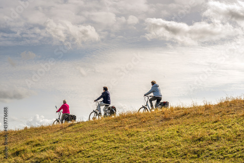 Canvas Print Three unidentified women cycle one behind the other with their electric bicycles on a Dutch dike