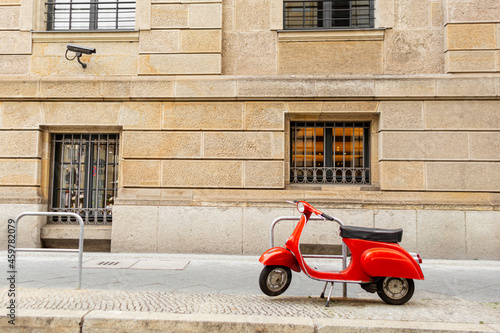 A stylish red moped is parked on a plain street. A bright spot in the city