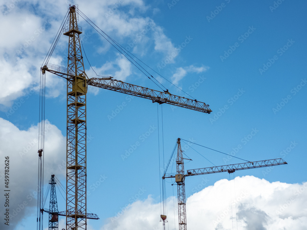 Tower cranes against a bright blue sky with clouds. Construction concept.