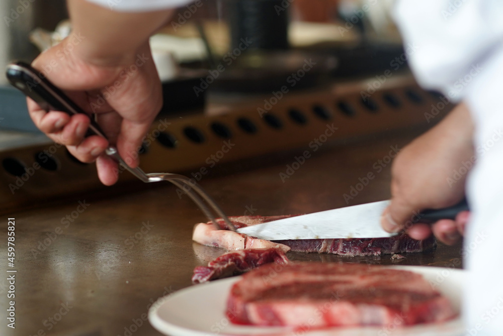 Chef trimming the excess fat from beef meat by a knife on a hot steel